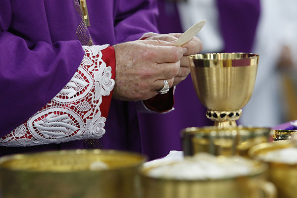 Archbishop Thomas Wenski prays over the consecrated bread and wine during an Ash Wednesday Mass at Archbishop McCarthy High School in 2016. Florida's bishops are trying to figure out how to resume the public celebration of Masses without contributing to the spread of the coronavirus or endangering the lives of parishioners who may become ill with COVID-19.