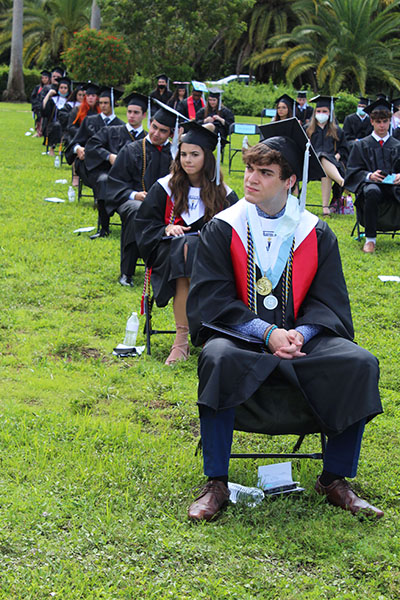 Dressed in cap and gown, and evenly spaced out, Archbishop Coleman Carroll High's graduating class of 2020 listen to remarks during their outdoor commencement ceremony held May 30, 2020 on school grounds.