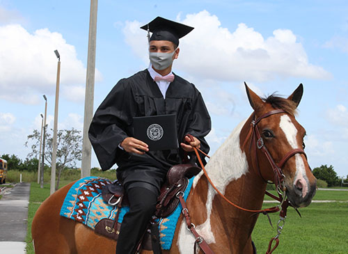 Arriving and departing by horseback, graduating senior Yancarlos Guerra from Archbishop Coleman Carroll High proudly displays his diploma after outdoor commencement ceremonies held on school grounds on May 30, 2020.