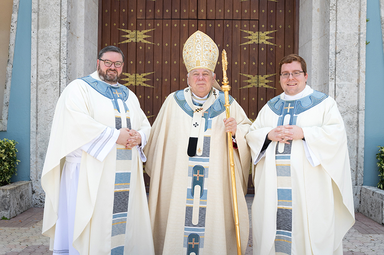 Newly ordained Father Ryan Saunders, left, and Father Andrew Tomonto, right, pose for a photo with Archbishop Thomas Wenski after the ceremony.
Archbishop Thomas Wenski ordained two South Florida natives to the priesthood for the Archdiocese of Miami June 27, 2020. The ceremony had been postponed from May due to the COVID-19 outbreak, and was still punctuated by mask-wearing and social distancing among the limited number of both faithful and priests in attendance.