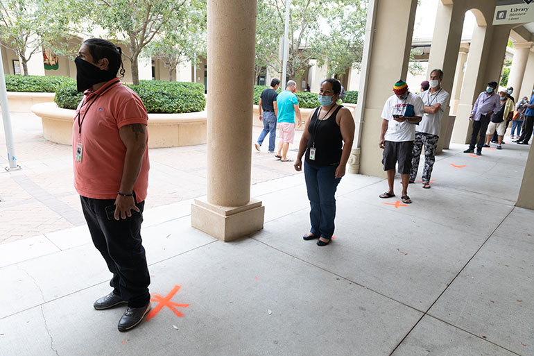 Para protegerse a sí mismos y a los demás durante la pandemia de COVID-19, los huéspedes residentes se alinean a seis pies de distancia para entrar al comedor de Camillus House, localizado en el centro de Miami.