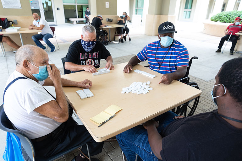 At Camillus House in downtown Miami, guests enjoy a game of dominos in the courtyard during the COVID-19 pandemic. To protect themselves and others, staff and resident guests at the homeless shelter are socially distancing, wearing face masks and stepping up sanitation and disinfection protocols. They are also finding additional ways to keep boredom at bay.