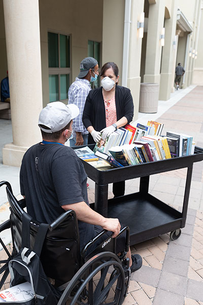 Hilda Fernandez, chief executive officer of Camillus House in downtown Miami, makes the rounds with a cart of donated books offered to residents who are staying here during the COVID-19 pandemic.