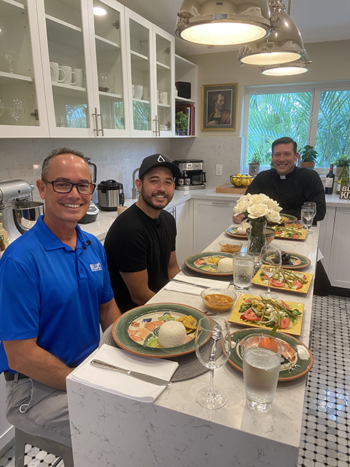 Father Richard Vigoa, rear, shares lunch with Jorge Rodriguez, left, and his son, Danny Rodriguez, during the filming of a June 4, 2020 episode of Bless This Kitchen at St. Augustine Church in Coral Gables. Danny Rodriguez co-founded BLUE Missions with his sister; their father now serves as chief growth officer.