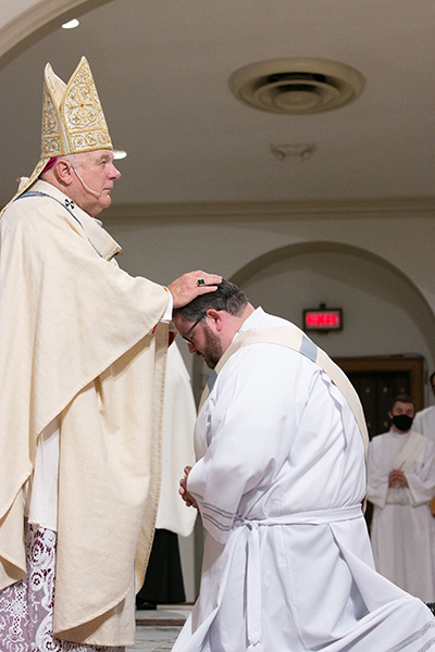 Archbishop Thomas Wenski lays hands on Deacon Ryan Saunders, ordaining him "a priest forever."
Archbishop Thomas Wenski ordained two South Florida natives to the priesthood for the Archdiocese of Miami June 27, 2020. The ceremony had been postponed from May due to the COVID-19 outbreak, and was still punctuated by mask-wearing and social distancing among the limited number of both faithful and priests in attendance.