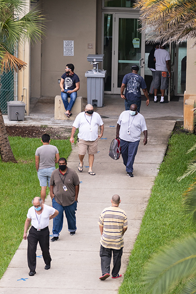 Residents, staff and guests at Miami's Camillus House shelter for the homeless in Miami move through the shelter's courtyard during a visit of the U.S. Surgeon General, Dr. Jerome Adams, July 23, 2020.