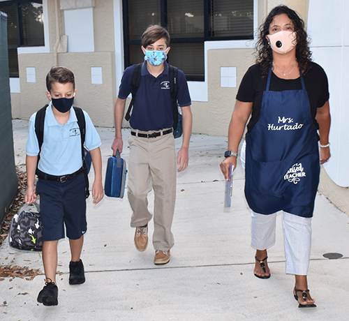 Teachers' assistant Diana Hurtado leads Michael Campanelli, 9, and his brother Nicholas, 12, to the gate of St. Bonaventure School on the first day of its study hall for children of essential workers, Aug. 24, 2020.