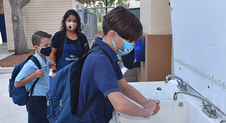 Nicholas Campanelli, 12, washes his hands at St. Bonaventure School before attending its study hall for children of essential workers. Teachers' assistant Diana Hurtado watches as brother Michael Campanelli, 9, waits his turn to wash, Aug. 24, 2020.