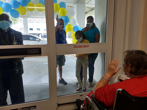 Father Parker Ogboe is seen here at left accompanying a family visiting their relative from behind the glass doors at Villa Maria Nursing Center in North Miami. The image was used in an August 2020 EWTN documentary on clergy ministering during the global pandemic. People in nursing homes are so vulnerable to COVID-19 that facilities throughout the U.S. have banned all visitors.