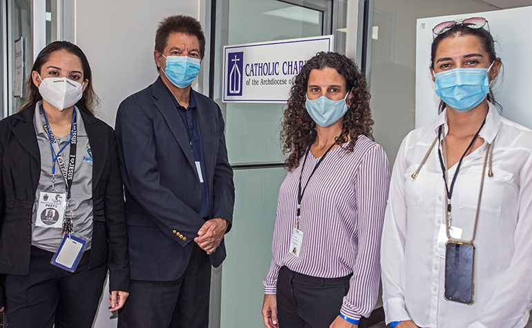 Posing at the entrance to the Malcolm Ross Senior Center in Allappatah, from left: Lourdes Ronces of Radio Paz; Peter Routsis-Arroyo, CEO of Catholic Charities; Iani Carvalho, the agency's regional director for Elderly Services; and Estephany Deleg, team leader for congregate meals.