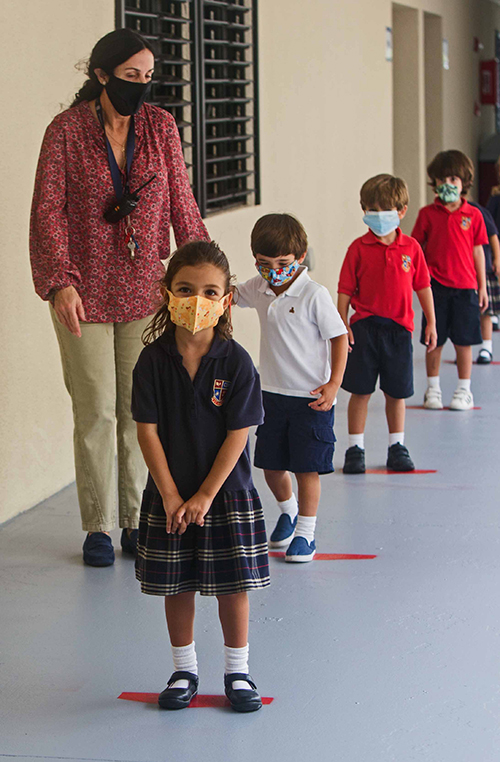 St. Hugh School pre-K4 teacher Rosy Medina shows Sebastian Reynal, 4, how to social-distance by standing on a red, six-foot line, as Isabel Barbera, 4, stands in front of him. Hans Hertell, 4, and Joaquin Maldonado, 4, are in line behind them.