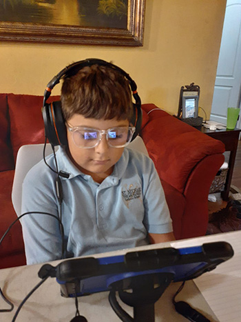 St. Michael the Archangel third grader Sabrian Fernandez is clad in his school uniform and wearing glasses to protect his eyes from the glare of the iPad as the 2020-2021 school year begins, online for now, Aug. 19, 2020.