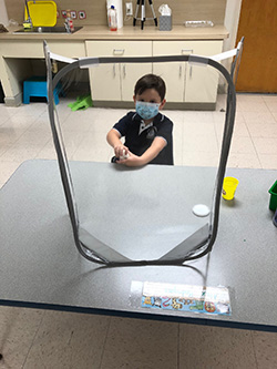 Alex Rodriguez, a PreK4 student at Mother of Our Redeemer School, Miami, is surrounded by a sneeze guard and wearing a mask on the first day of school, Aug. 19, 2020.