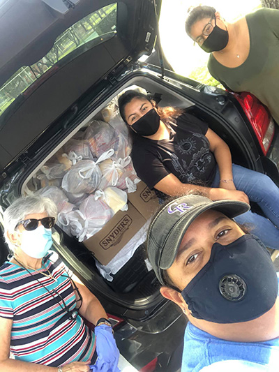 With face masks on and a trunk full of food, La Salle Educational Center team Silvia Munoz, Monica Lauzurique, Dulce Olivera, and Yancy Velasquez pose for a selfie before distributing food donations door to door in the South Dade Labor Camp, where 300 units are the homes of adults, families with children and elderly.