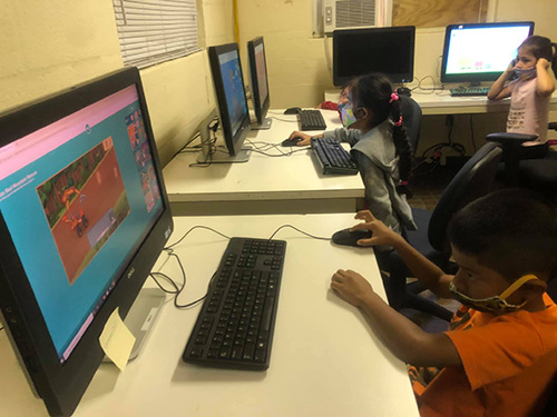 Con máscaras faciales, los niños del Centro Educativo La Salle utilizan las computadoras para aprender y jugar durante el campamento de verano 2020.