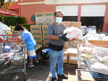 César Coronado, ministro laico de la iglesia Mother of Christ, en Miami y Nancy Bohnenblust, una entusiasta voluntaria, colocan las bolsas de alimentos en los autos que avanzan en una larga fila.