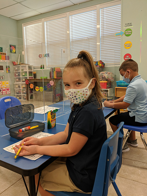 Abigail Kyer, in Kindergarten, settles into her new desk on the first day of the 2020 academic year at The Basilica School of St. Mary Star of the Sea, wearing her colorful face mask.