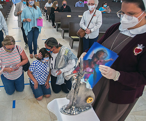 Lidia Navarrete kisses her grandson, Randy Medina, 11, as his mother, Miriam Medina, kneels beside them, and Sister Evelyn Montes de Oca, of the Servants of the Pierced Hearts of Jesus and Mary, touches a picture of St. John Paul II to his relic. Pilgrims venerated the relics of St. John Paul II at Our Lady of Guadalupe Church, Doral, on his feast day and the 100th anniversary of his birth, Oct. 22, 2020.