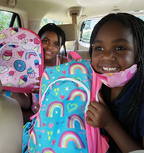 Two of the 175 recipients show off the backpacks they got at Hope, Heart & Home ministry's Aug. 8, 2020 giveaway at St. John Neumann Church in Miami.