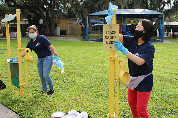 Before painting, Solanghe Rodriguez and Adriana Kambe wipe down playground equipment at Catholic Charities of the Archdiocese of Miami's Notre Dame Child Development Center in Little Haiti, Nov. 5, 2020. The two, who work with the accounting and advising firm Hancock, Askew and Co., volunteered for a service day.