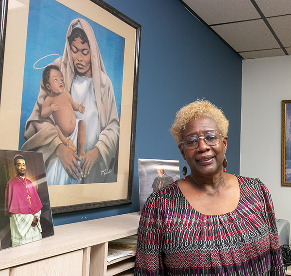 Katrenia Reeves-Jackman, directora de la Oficina arquidiocesana del Ministerio Católico Negro, posa delante de un cuadro de una Virgen negra y un niño. El cuadro de la izquierda es de un obispo muy joven, ahora Cardenal electo Wilton Gregory de Washington, D.C., el primer afroamericano en llegar a ese rango.