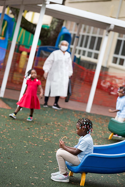 Staff clad in personal protective equipment look on as youngsters enjoy recess at the Catholic Charities-sponsored child development center/Head Start program at Holy Redeemer Church in Miami. It is one of six such programs throughout Miami-Dade County operating at reduced in-class capacity during the COVID-19 global pandemic.