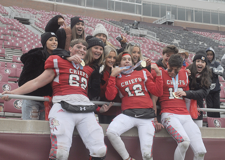 Cardinal Gibbons senior players (from left) William Spicer, Brody Palhegyi and Troy Stellato hold up their medals with fans while celebrating the Chiefs' 35-21 victory over Jacksonville Bolles on Thursday, Dec. 17, 2020, in the Class 4A FHSAA State Football Championship Game at Bobby Bowden Field at Doak Campbell Stadium in Tallahassee.