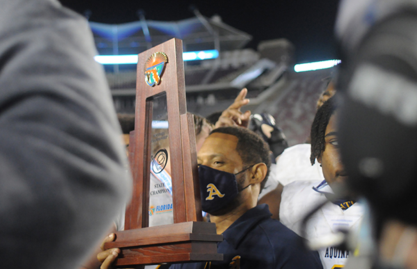 St. Thomas Aquinas coach Roger Harriott holds onto the trophy while celebrating the Raiders' 31-21 victory over Orlando Edgewater, Dec. 19, 2020, in the FHSAA Class 7A Football State Championship Game at Bobby Bowden Field at Doak Campbell Stadium. The Raiders won their state-record 12th title.