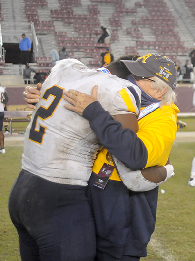 Athletic director George Smith hugs senior captain Tyreak Sapp as other players celebrate St. Thomas Aquinas' 31-21 victory over Orlando Edgewater, Dec. 19, 2020, in the FHSAA Class 7A Football State Championship Game at Bobby Bowden Field at Doak Campbell Stadium. The Raiders won their state-record 12th title.