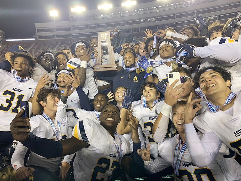 Coach Roger Harriott joins his players with the trophy in celebrating St. Thomas Aquinas' 31-21 victory over Orlando Edgewater, Dec. 19, 2020, in the FHSAA Class 7A Football State Championship Game at Bobby Bowden Field at Doak Campbell Stadium. The Raiders won their state-record 12th title.