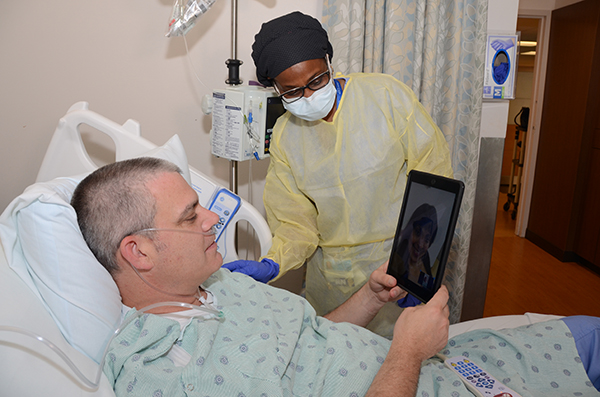 A nurse helps a patient speak to relatives via video call in the midst of the COVID-19 pandemic. Holy Cross is taking part in two clinical trials to gauge whether some therapies lessen the complications associated with COVID-19, the illness caused by the coronavirus.
