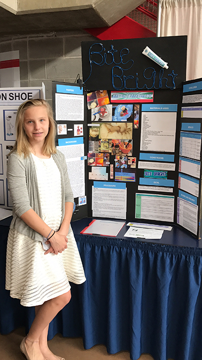 Nikita Marino poses by her presentation board of the Bite Bright fluoride-free toothpaste she invented in the seventh grade. Nikita, who is a junior at Immaculata La Salle, received a patent from the U.S. Patent and Trademark Office for her product in November 2020.