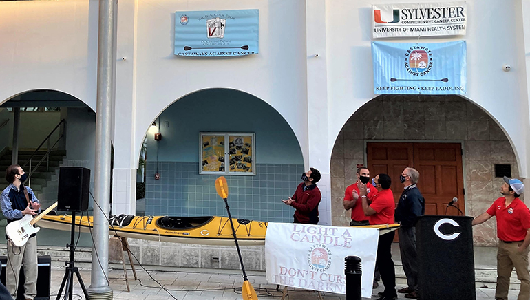 Teachers and alumni of Christopher Columbus High School look on as the new logo for Castaways Against Cancer is unveiled, Feb. 4, 2021. From left, standing at bottom: Javier Hermedia, Adam Scholer, Jose Mendoza, Paul Kumer, and Castaways captain Eric Pino (at podium).