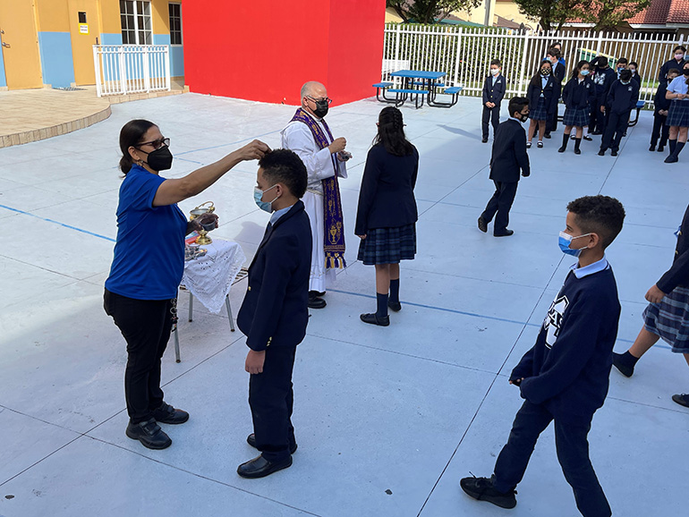 Father Juan Hernandez, pastor, and Altagracia Batista, preK aide, distribute ashes to students at Mother of Our Redeemer School, Feb. 17, 2021.