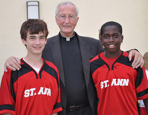 Father Seamus Murtagh is pictured in this file photo visiting with Andrew Floering, left, and Max-Oliver Ducoste-Amedee, students at St. Ann School in West Palm Beach.