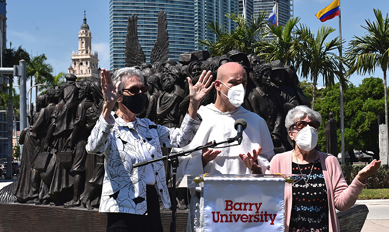 Leaders of Barry University lead a Dominican prayer in Miami during the announcement of the university's new Institute for Immigration Studies. From left are Sister Mary Anne Caulfield, regional superior of the Adrian Dominican Sisters; Father Cristobal Torres, campus chaplain at Barry; and Sister Linda Bevilacqua, past president of the university. Behind them is the sculpture "Angels Unawares," on display at Bayfront Park.