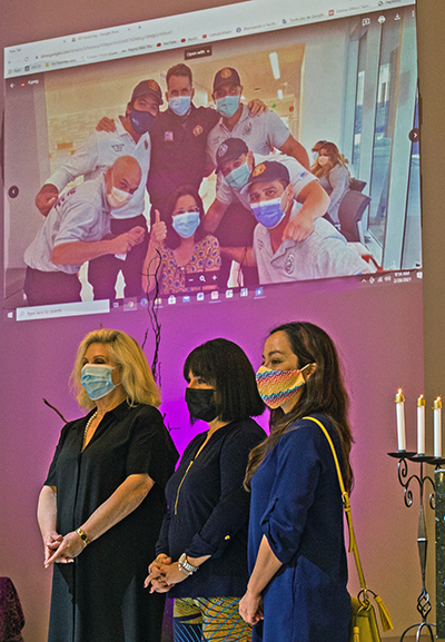 Jackson Memorial Hospital representatives stand below a photo of JMH workers while listening to Father Federico Capdepon's words of gratitude during a Mass Feb. 28, 2021 at Corpus Christi Church in Miami. From left: Mariana Martinez, chairperson of JMH International Children's Fund; Maylen Montoto, associate director of Events and Sponsorship Sales for JMH's Community Foundation; and Madeline Barrios, community outreach manager at Jackson Health System.