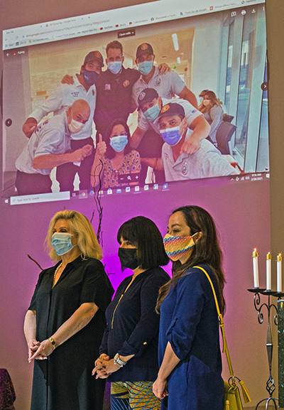 Los representantes del Jackson Memorial Hospital escuchan, debajo de una foto de los trabajadores de JMH, las palabras de gratitud del P. Federico Capdepón, durante una Misa el 28 de febrero de 2021, en la iglesia Corpus Christi en Miami. Desde la izquierda: Mariana Martínez, del Consejo Asesor de IKF Wonderfund; Maylen Montoto, directora asociada de Ventas de Eventos y Patrocinio de Jackson Health Foundation; y Madeline Barrios, gerente de alcance comunitario en Jackson Health System.