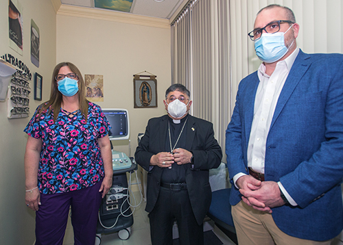 Rosita Porras, técnica de ultrasonido; el Obispo Auxiliar Enrique Delgado; y Mario Labella, director ejecutivo de Strena Medical, posan para una foto después de que el Obispo bendijera la nueva máquina de ultrasonido para el Centro de ayuda para el embarazo de North Broward, el 3 de marzo de 2021.