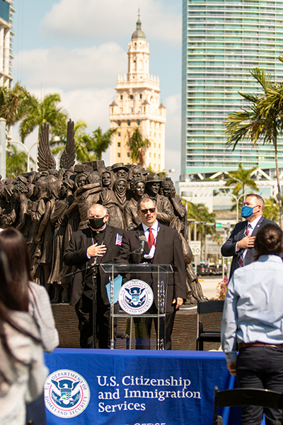 Gustavo Zayas, director de música de la Arquidiócesis, canta el himno nacional al inicio de la ceremonia celebrada junto a la escultura "Ángeles sin saberlo" y con la Torre de la Libertad de Miami atrás, el 24 de marzo de 2021.