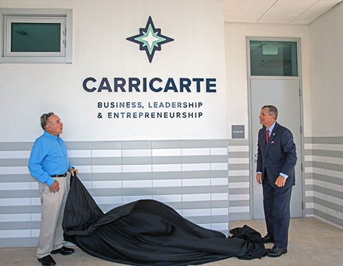 Michael Carricarte, Sr., and Juan Vila, academic dean at Christopher Columbus High School, unveil the Carricarte Business, Leadership and Entrepreneurship logo outside the business classroom April 15, 2021. The family of alums gave its name and support to the business career pathway at the all-boys Miami high school.