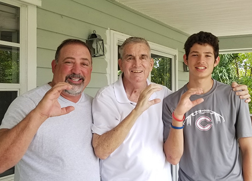 Raul Rivero, left, Christopher Columbus class of 1984, and his son, Raul Jr., a current junior at the Miami high school, throw up the Columbus "C" with Father Arthur Dennison during a visit with the priest in mid-April, just a few days before his April 23, 2021 death at the age of 74.