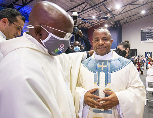 Newly ordained Father Franklin Ekezie wears his priestly vestments after being vested by a fellow Nigerian who welcomed him into his parish, Father Samuel Muodiaju, left, pastor of St. Monica in Miami Gardens.