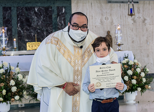 Father Matthew Gomez gives a Miami Serra Club altar server award to Maximiliano Cacchione, 7, one of four siblings who serve at Mass every day except Saturday at St. Augustine Church in Coral Gables. Father Gomez, chaplain of the Miami Serra Club and archdiocesan vocations director, celebrated the awards Mass May 15, 2021 at St. John Vianney College Seminary in Miami.
