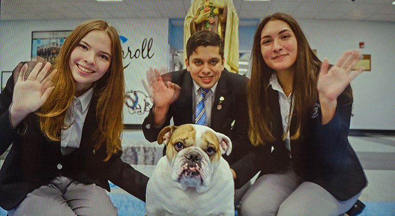 Offering greetings from their school in a loop that ran before the start of the baccalaureate Mass, from left: Archbishop Coleman Carroll High's Elizabeth Fitzgerald, 18, valedictorian; Daniel Valdez, 19, Archbishop's Leadership Award winner; Camila Gloria, 18, salutatorian, and the school's bulldog mascot, Archie. Representatives of nine of the 12 Catholic high schools in the Archdiocese of Miami took part in the Mass, celebrated by Archbishop Thomas Wenski May 24, 2021 at St. Mary Cathedral.