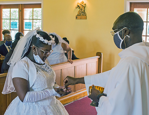 Father Fidelis Nwankwo, administrator of St. Philip Neri Parish, gives first Communion to Emari Miller, 11, during Mass on Trinity Sunday, May 30, 2021.