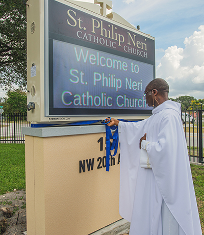 Father Fidelis Nwankwo, St. Philip Neri Church administrator, cuts the ribbon on the church's new digital sign on Trinity Sunday, May 30, 2021.