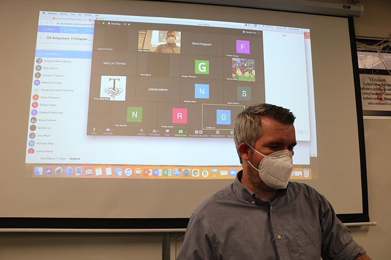 Brian Dunne teaches history to a class of juniors during sessions at Cardinal Gibbons High School May 25, 2021. The screen behind him reveals online students participating in class alongside the students sitting in the classroom.