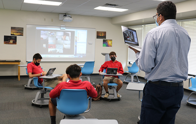 Nelson Araque moves about his classroom talking and asking questions to the students sitting in front of him as well as those connected virtually online. He is busy multitasking through the entire session trying to keep the class interesting and his students engaged.