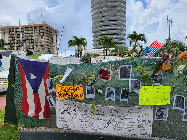 Filled with pictures, flowers, rosaries, and words of comfort, a temporary memorial for the missing and for the victims of the Champlain Towers South condominium (on the left) was erected on the sidewalk of Stella Maris House, behind St. Joseph Church. The memorial was relocated on the evening of July 1, 2021, and added to the larger memorial at the tennis court across the street from the collapsed building.